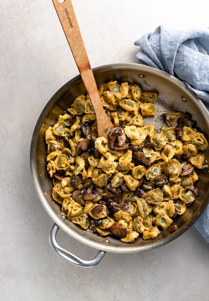 Skillet filled with cooked tortellini with mushrooms and Parmesan.