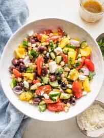 White serving bowl filled with a Greek chickpea salad containing bell pepper, cucumber, tomato, olives, red onion, and feta cheese.