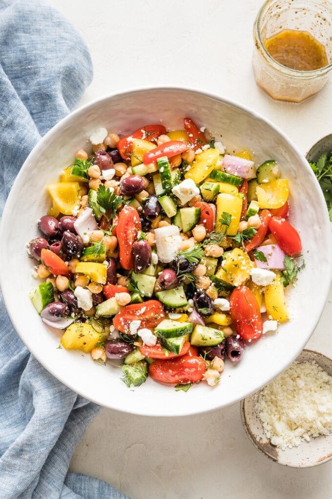 White serving bowl filled with a Greek chickpea salad containing bell pepper, cucumber, tomato, olives, red onion, and feta cheese.