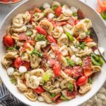 Close up of a bowl full of tortellini pasta salad loaded with peppers, pepperoni, tomatoes, mozzarella, and Italian dressing.