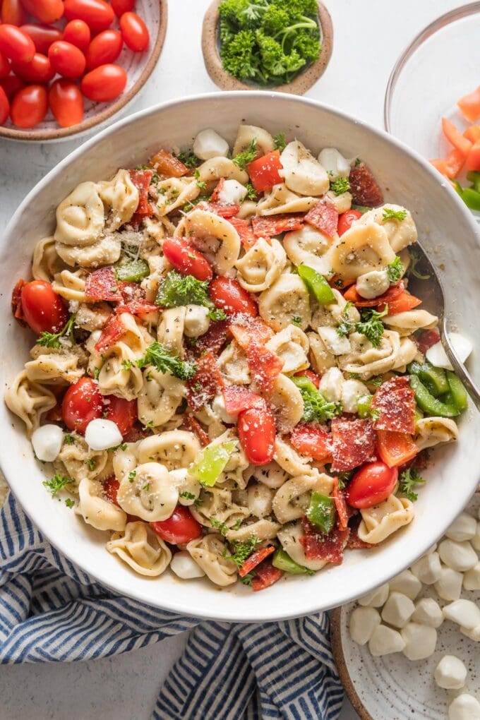 Close up of a bowl full of tortellini pasta salad loaded with peppers, pepperoni, tomatoes, mozzarella, and Italian dressing.