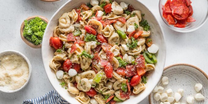 Close up of a bowl full of tortellini pasta salad loaded with peppers, pepperoni, tomatoes, mozzarella, and Italian dressing.