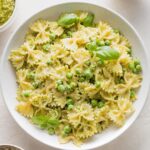 Bowl full of pesto pasta and peas garnished with extra Parmesan and fresh basil leaves.