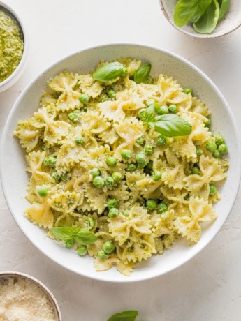 Bowl full of pesto pasta and peas garnished with extra Parmesan and fresh basil leaves.