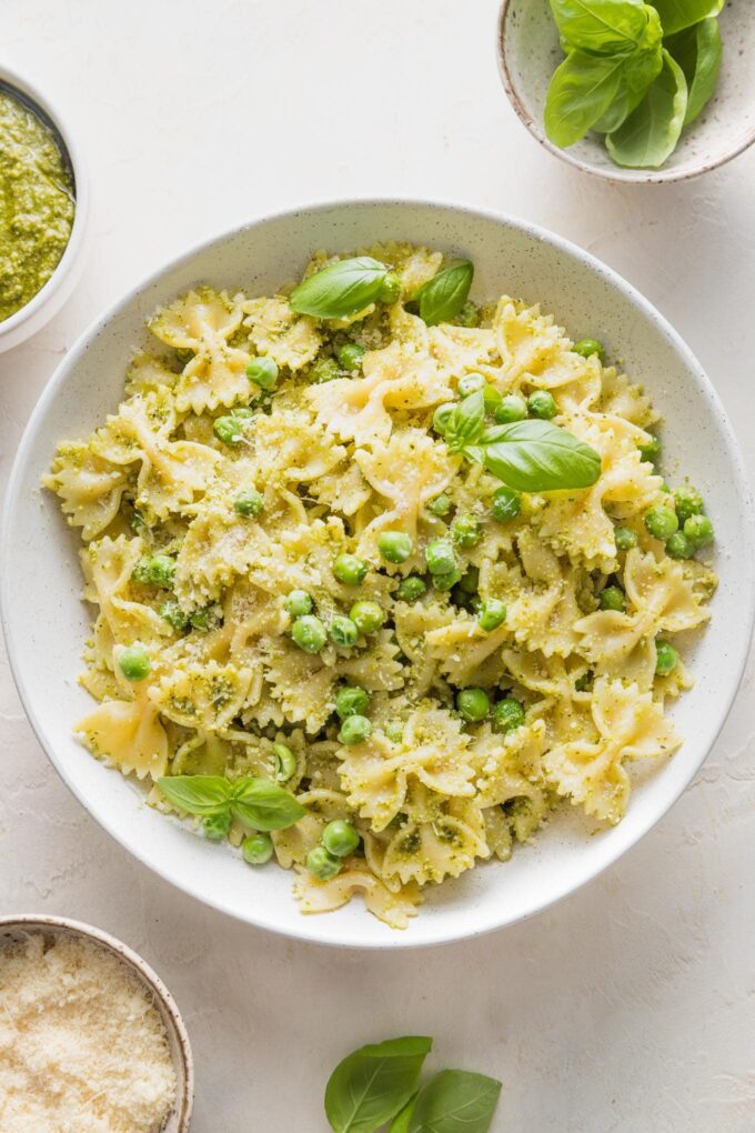 Bowl full of pesto pasta and peas garnished with extra Parmesan and fresh basil leaves.