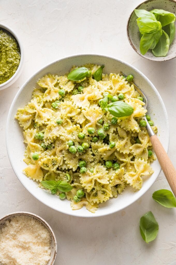 Bowl full of pesto pasta and peas garnished with extra Parmesan and fresh basil leaves.