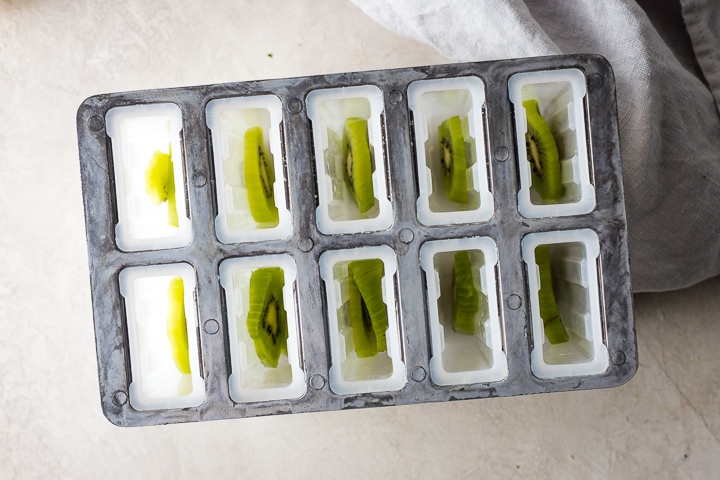 Popsicle molds with kiwi slices inside.