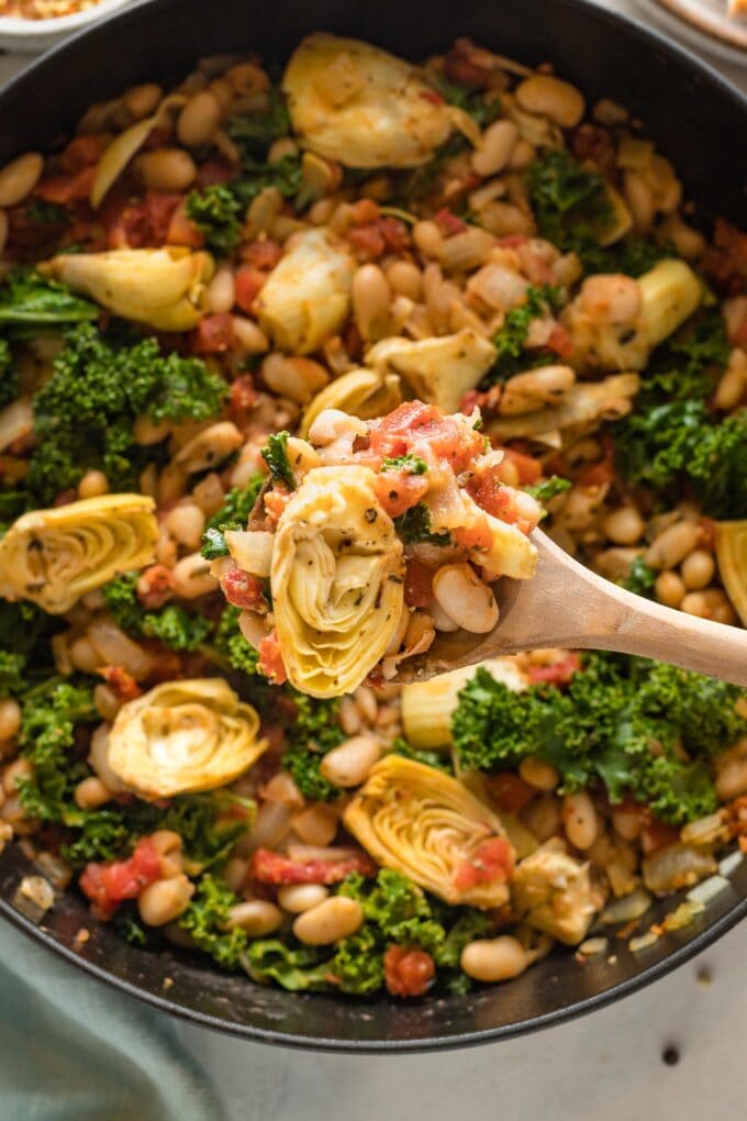 Close up of white beans cooked with kale, artichokes, and sun-dried tomatoes.