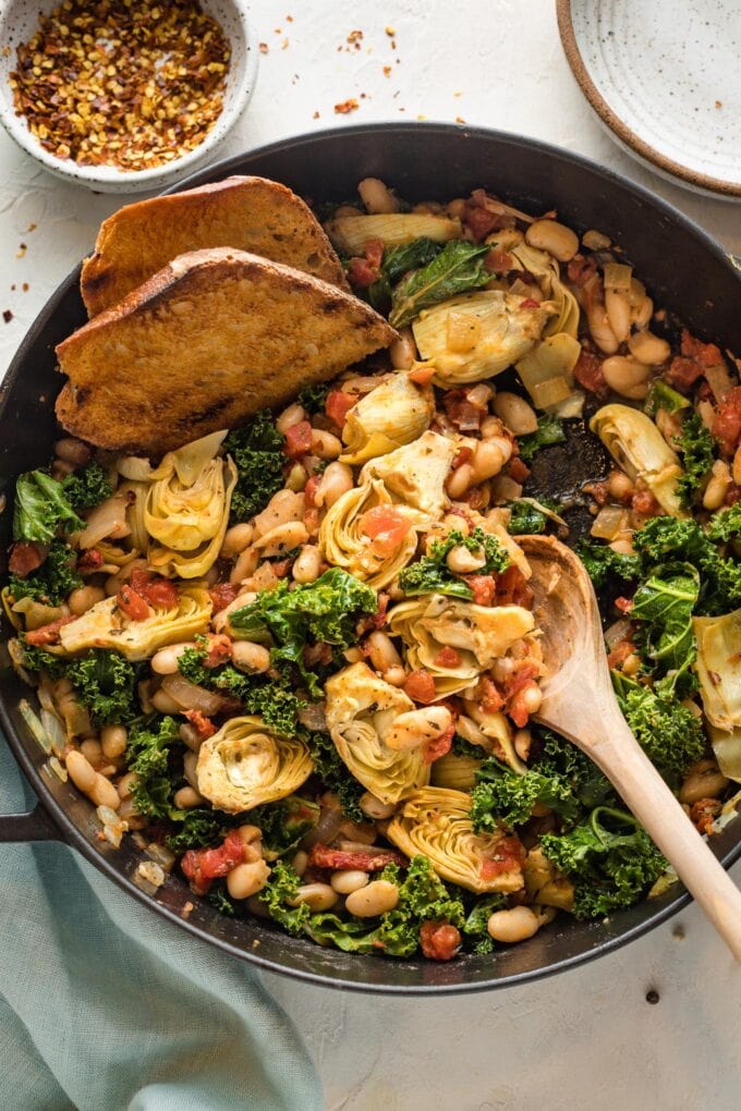 Close up of a serving spoon in a Tuscan white bean skillet.