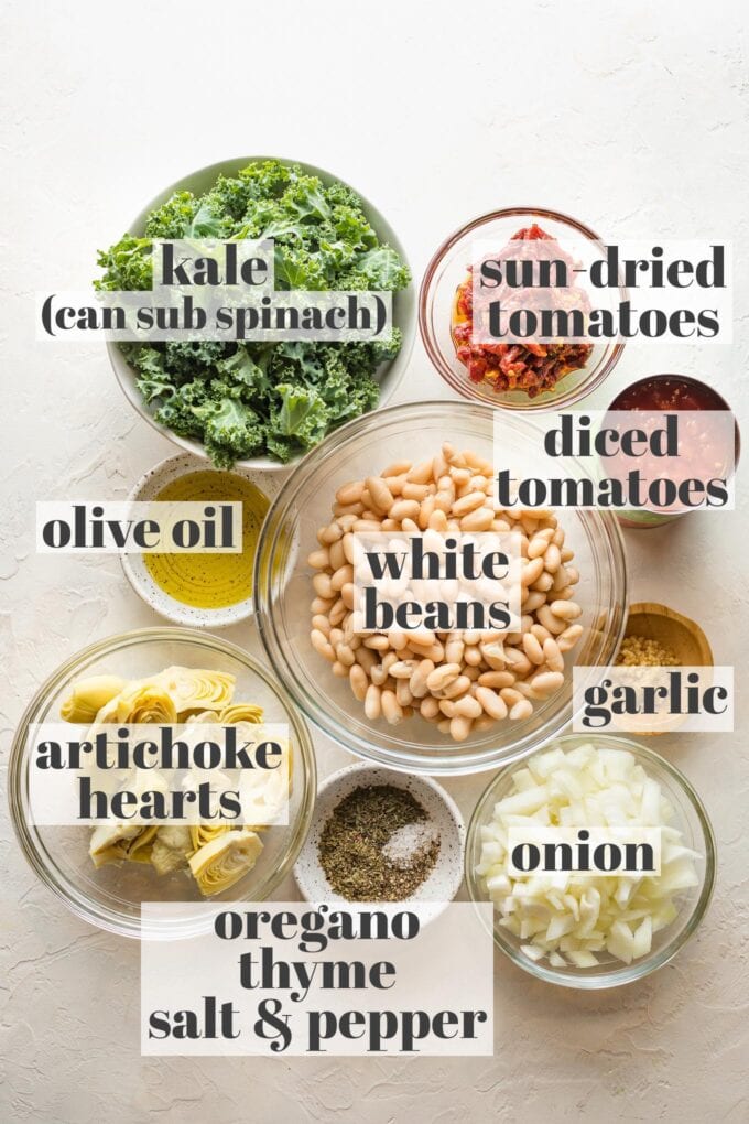 Labeled photo of prep bowls holding kale, sun dried tomatoes, white beans, diced tomatoes, minced garlic, chopped onion, olive oil, artichoke hearts, and spices.