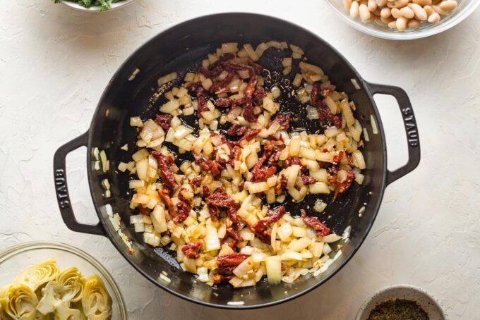 Onion and sun-dried tomatoes cooking in a cast iron skillet.