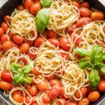 Overhead image of a skillet holding spaghetti with roasted tomatoes, Parmesan, and fresh basil.