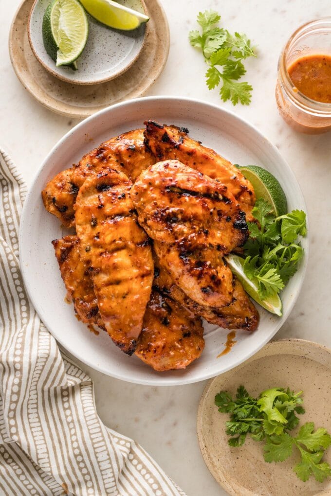 Plate with honey chipotle chicken garnished with cilantro leaves and fresh lime wedges.