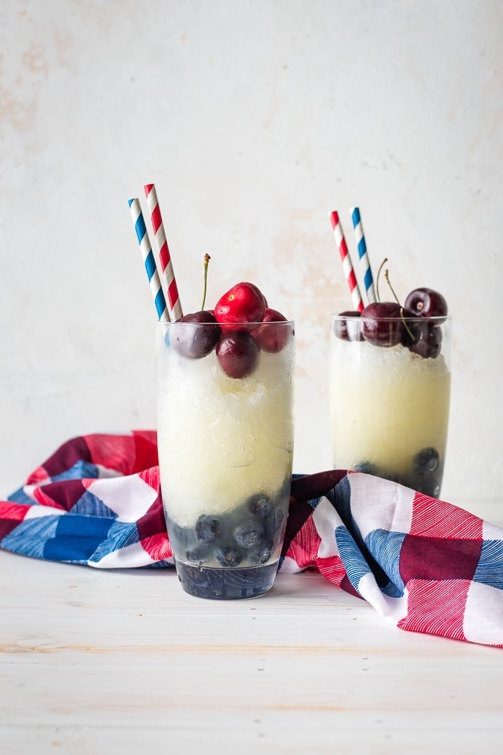 Two glasses filled with layered red, white, and blue frozen lemonade.