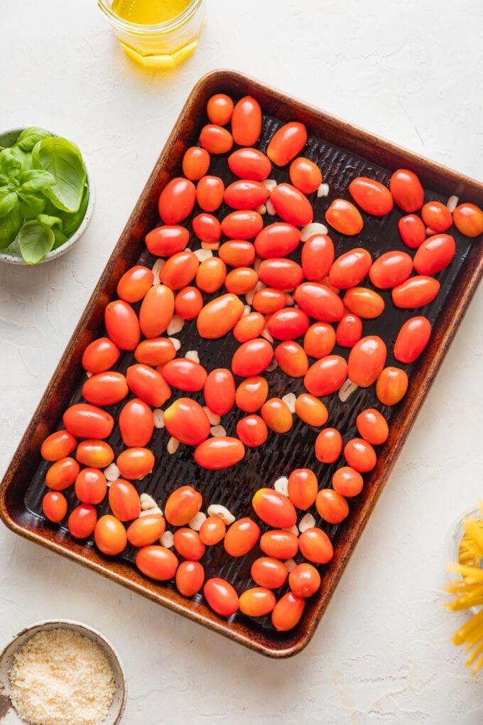Rimmed sheet pan holding cherry tomatoes, sliced garlic, and drizzled olive oil.