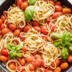 Overhead image of a skillet holding spaghetti with roasted tomatoes, Parmesan, and fresh basil.