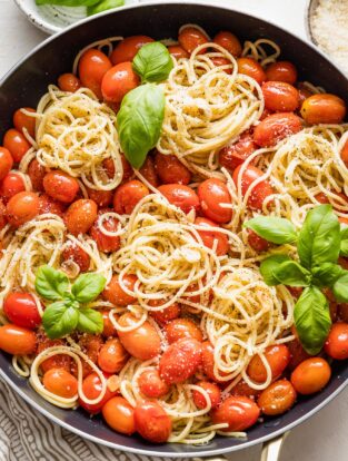 Overhead image of a skillet holding spaghetti with roasted tomatoes, Parmesan, and fresh basil.