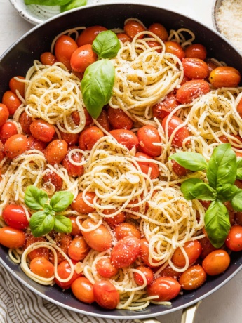 Overhead image of a skillet holding spaghetti with roasted tomatoes, Parmesan, and fresh basil.