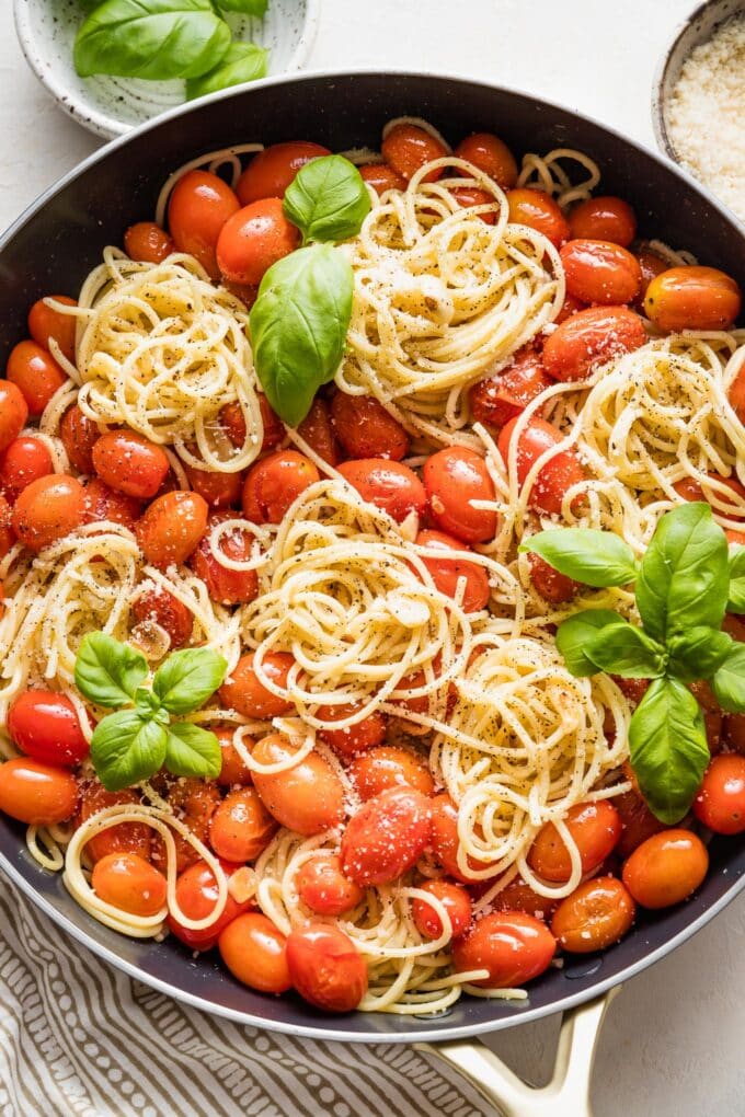 Overhead image of a skillet holding spaghetti with roasted tomatoes, Parmesan, and fresh basil.