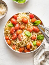 A small bowl containing roasted tomato pasta garnished with fresh basil and Parmesan, ready to eat.