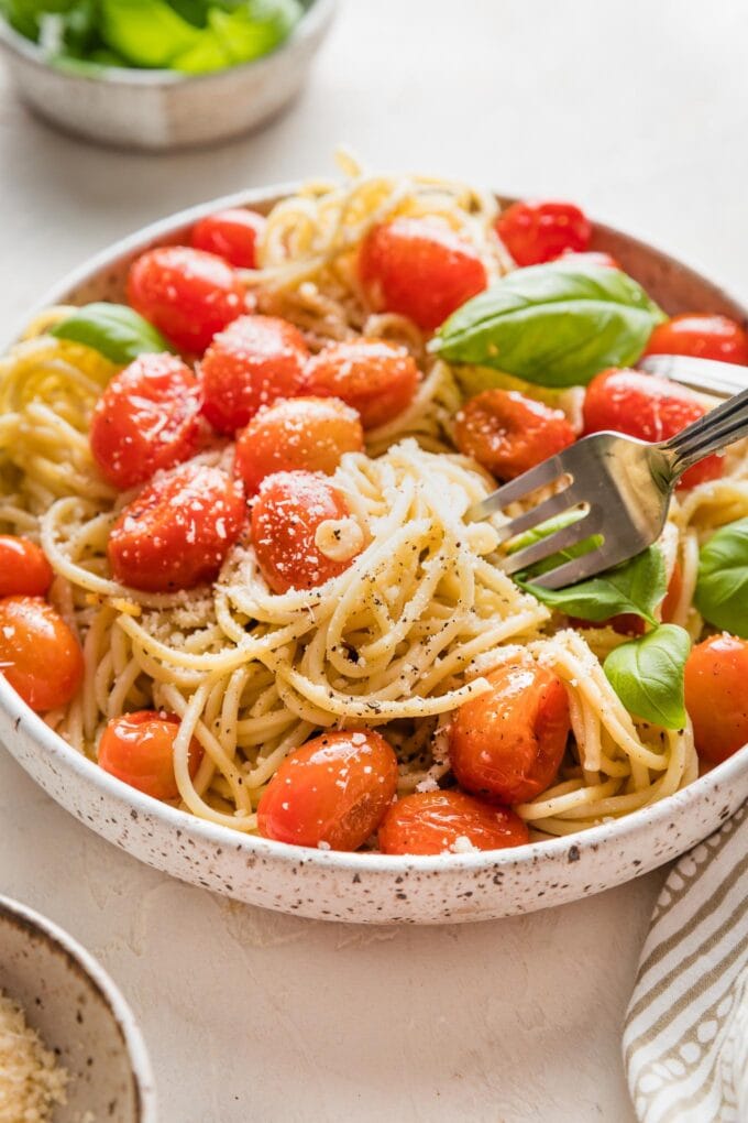 Close-up image of a fork twirling spaghetti around with roasted cherry tomatoes and fresh basil.