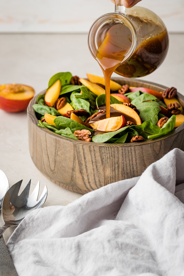 Close up image of a mustard balsamic vinaigrette dressing being poured on a spinach salad.