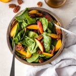 A bowl of spinach salad with nectarines and pecans.