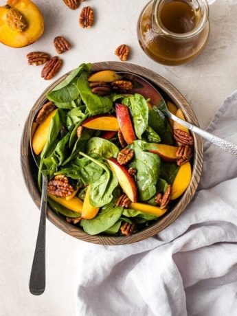 A bowl of spinach salad with nectarines and pecans.
