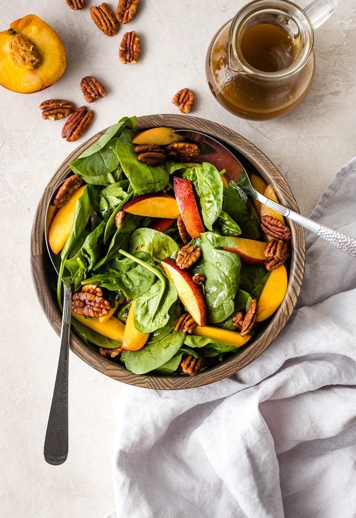 A bowl of spinach salad with nectarines and pecans.