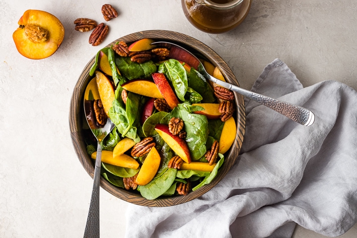 A bowl of spinach salad with nectarines and pecans.