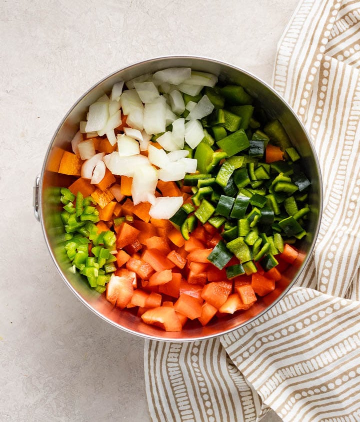 A mixing bowl filled with chopped onion, jalapeno, poblano, and bell peppers.