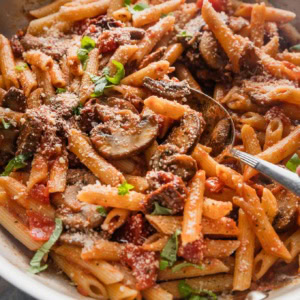 Large skillet full of penne alla vodka with mushrooms, sun-dried tomatoes, fresh basil, and Parmesan.