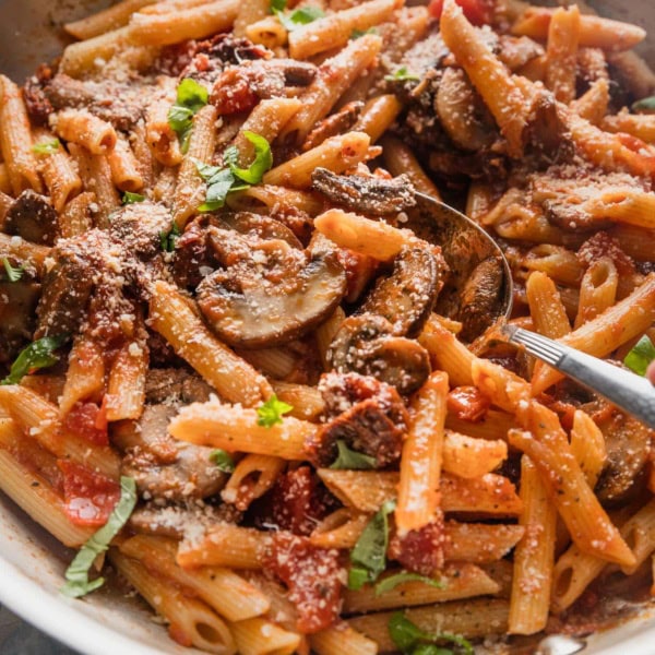 Large skillet full of penne alla vodka with mushrooms, sun-dried tomatoes, fresh basil, and Parmesan.
