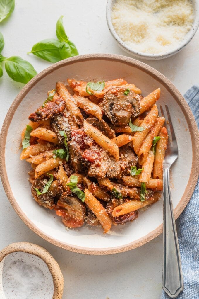 Close up of a counter set with a bowl of vegetarian vodka pasta with fresh basil and Parmesan.