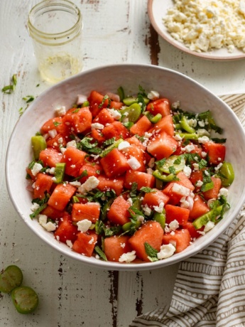 A large serving bowl of fresh watermelon salad with tomatillos, jalapenos, and lime dressing.