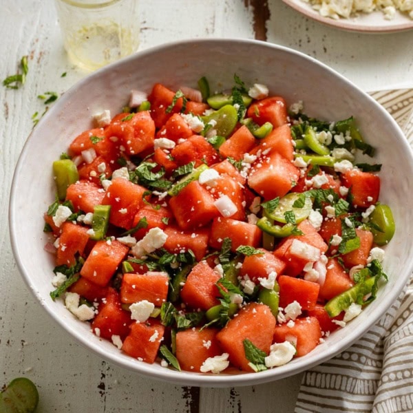 A large serving bowl of fresh watermelon salad with tomatillos, jalapenos, and lime dressing.
