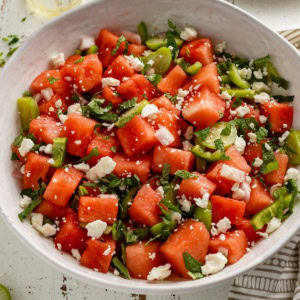 A large serving bowl of fresh watermelon salad with tomatillos, jalapenos, and lime dressing.