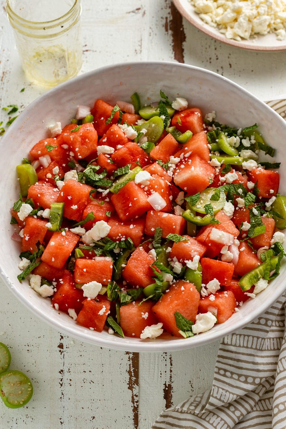 A large serving bowl of fresh watermelon salad with tomatillos, jalapenos, and lime dressing.