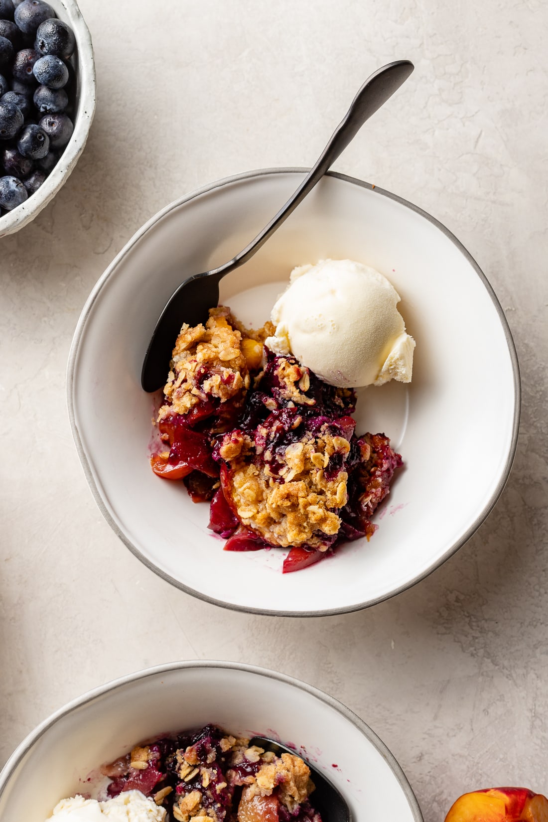 A serving bowl filled with blueberry nectarine crisp and a scoop of vanilla ice cream.