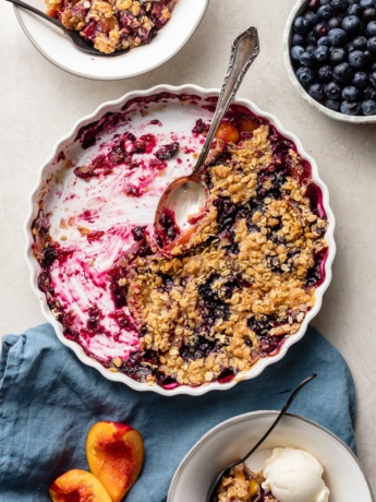 Half-eaten blueberry nectarine crisp, scraped out of a white baking dish.