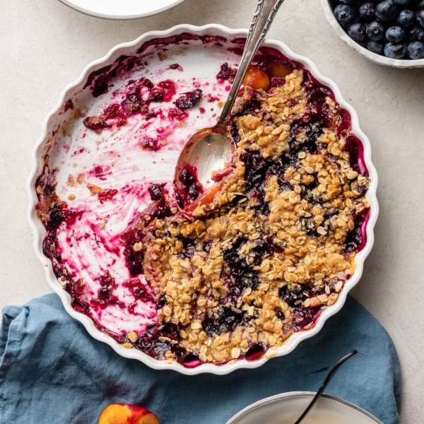 Half-eaten blueberry nectarine crisp, scraped out of a white baking dish.