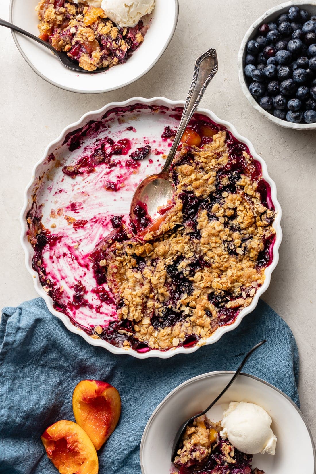Half-eaten blueberry nectarine crisp, scraped out of a white baking dish.