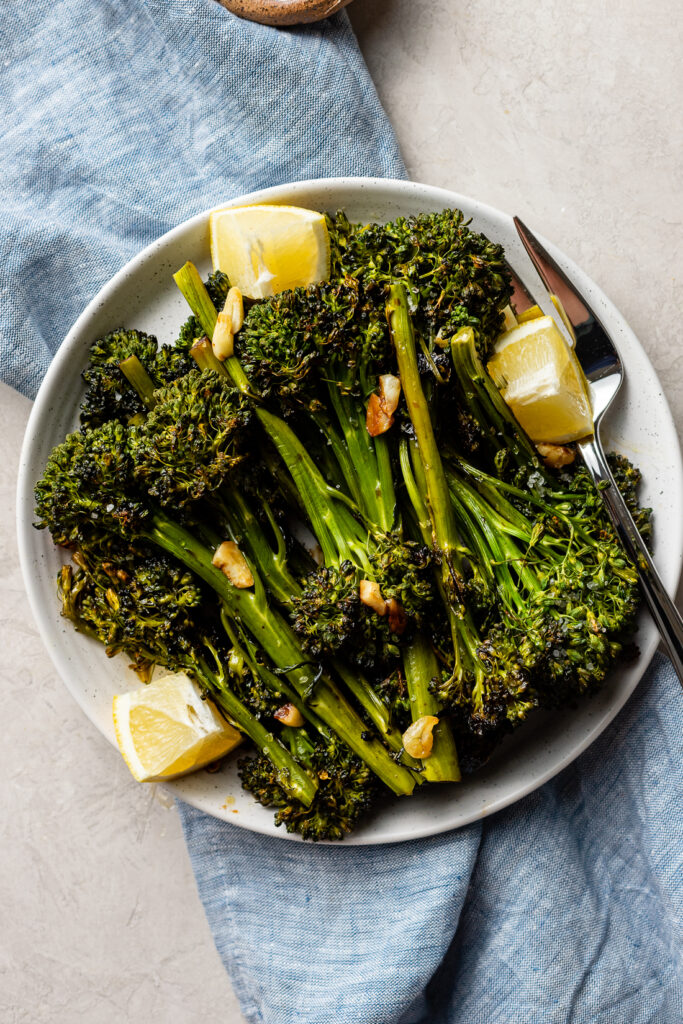 A plate of oven-roasted broccolini with soy sauce, garlic, salt, and lemon wedges.