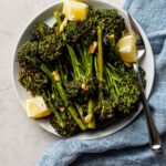 A plate of oven-roasted broccolini with soy sauce, garlic, salt, and lemon wedges.