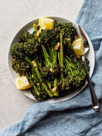 A plate of oven-roasted broccolini with soy sauce, garlic, salt, and lemon wedges.
