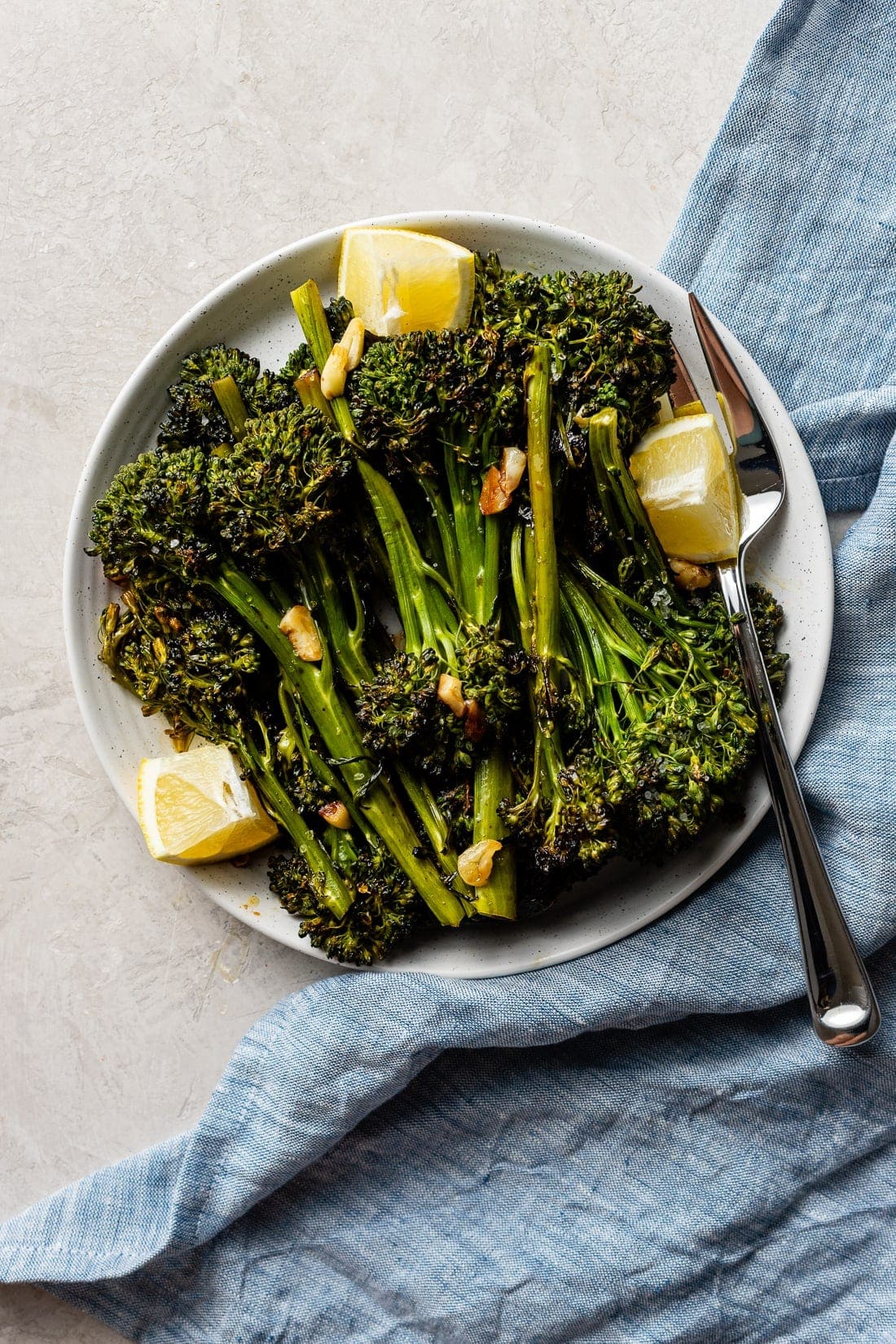 A plate of oven-roasted broccolini with soy sauce, garlic, salt, and lemon wedges.