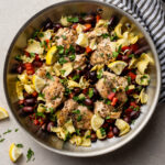 Skillet filled with Greek chicken with olives, tomatoes, and artichokes.