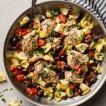 Skillet filled with Greek chicken with olives, tomatoes, and artichokes.