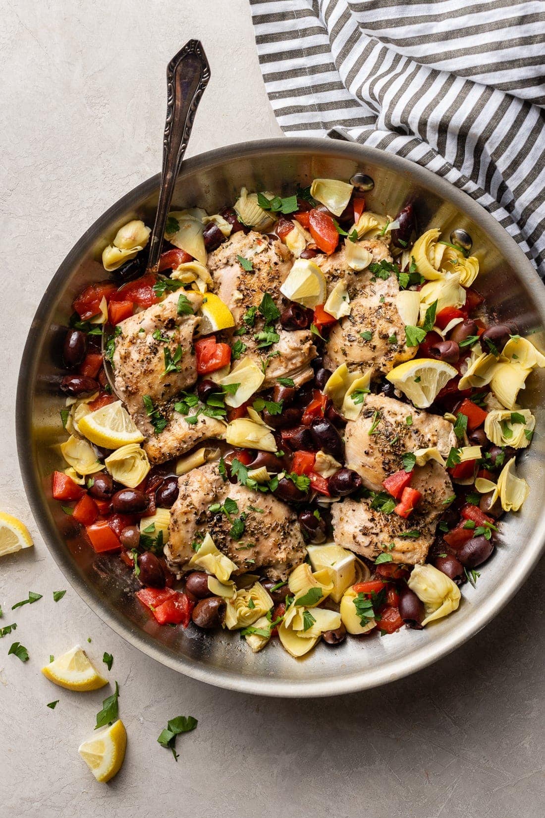 Skillet filled with Greek chicken with olives, tomatoes, and artichokes.