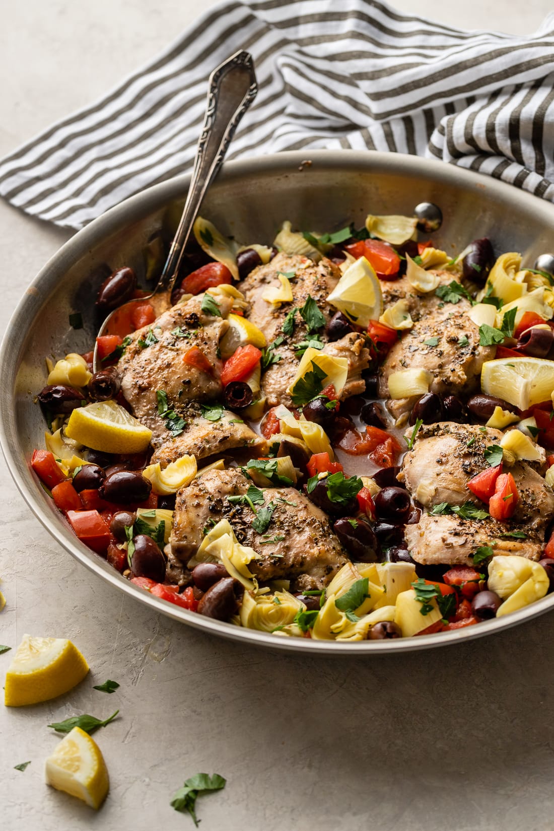 Skillet filled with Greek chicken with olives, tomatoes, and artichokes.